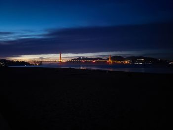 Illuminated city by sea against sky at night