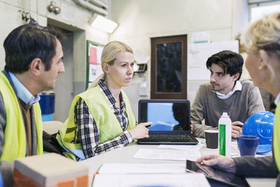 Female worker showing something on laptop to colleagues in factory