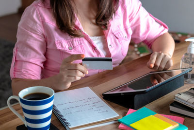 Midsection of woman holding smart phone while sitting on table