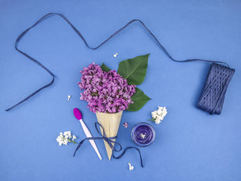 Lilac flowers in a wooden cone, paper tape, cosmetic cream and a brush for masks on a blue.