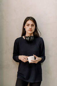 Portrait of businesswoman with cup against wall in office