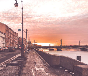 Street by sea against sky at sunset