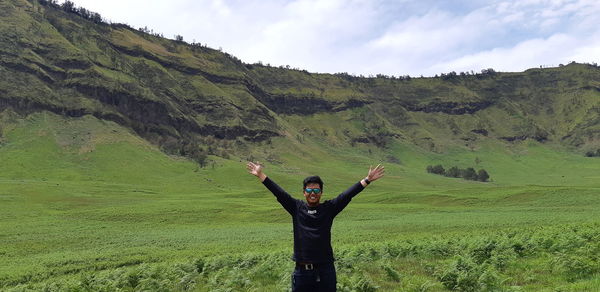 Man with arms raised on field against sky