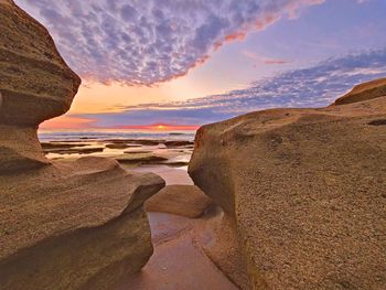 Rocks on beach against sky during sunrise