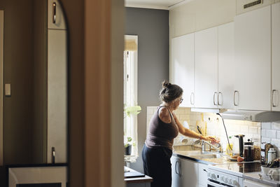 Side view of woman with disability turning off faucet while working in kitchen at home