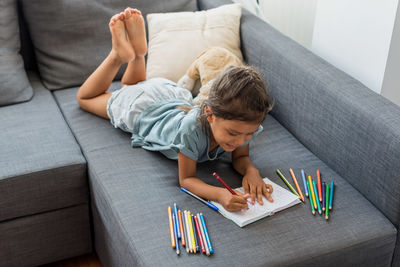 Hispanic girl painting on a sofa with pencil colors.