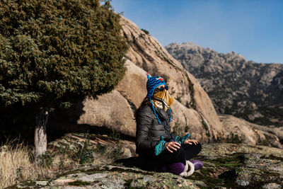 Man sitting on rock by mountains against sky