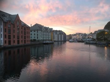 Buildings by river against sky during sunset