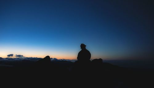 Silhouette man standing on cliff against clear blue sky