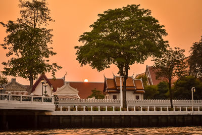 Building by trees against sky during sunset