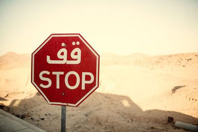 Close-up of road sign on sand against clear sky