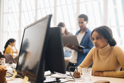 Focused businesswoman using computer while coworkers working in background at office