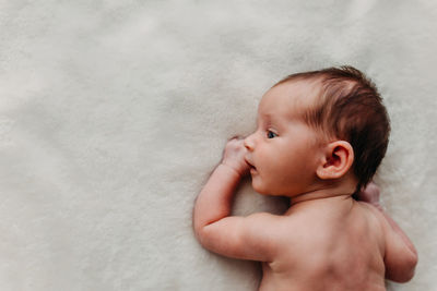 Newborn baby laying on a white blanket and looking to the side