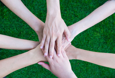 Cropped image of people stacking hands against grass