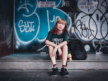 Portrait of teenage girl sitting on graffiti