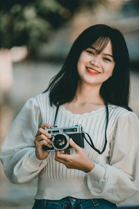 Portrait of smiling young woman holding camera