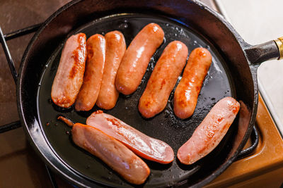 Half-cut sausages are fried in oil in a black cast iron skillet