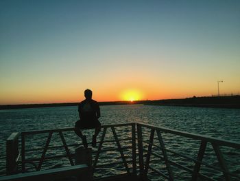 Rear view of silhouette man standing on railing against sea