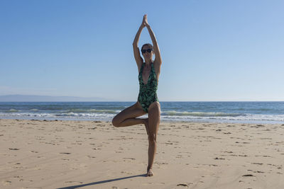 Doing yoga at the beach, the girl practices the yoga tree pose, the harmony of the body with nature.