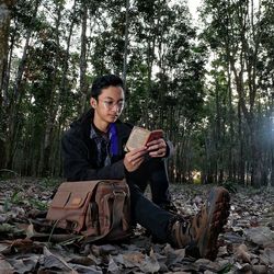 Young man reading book while sitting in forest