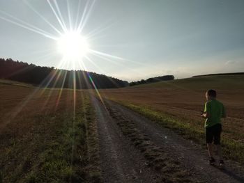 Rear view of man standing on field against bright sun