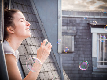 Side view of woman blowing bubbles from window