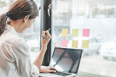 Midsection of woman working with laptop in window