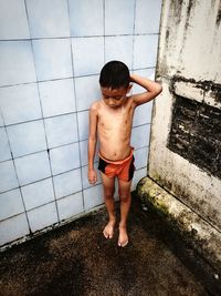 Full length of shirtless boy showering against tiled wall