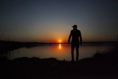 Rear view of silhouette man standing at beach during sunset