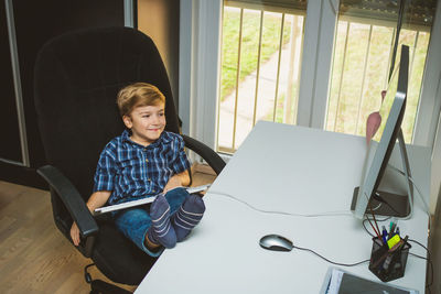 High angle view of cute boy using computer on desk at home