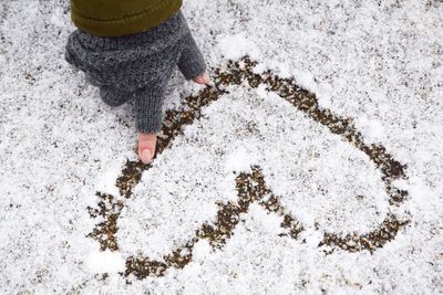 Cropped hand of woman wearing fingerless glove while making heart shape on snow during winter