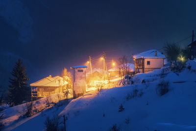 Snow covered houses by buildings against sky at night