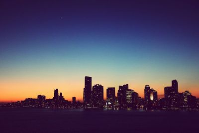 Silhouette buildings by sea against sky during sunset