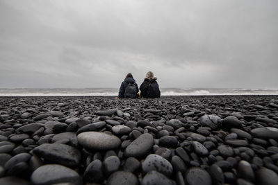 People on rocks at beach against sky