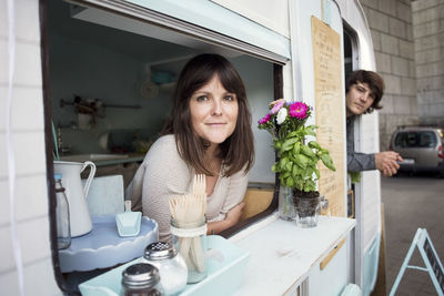 Portrait of male and female owners leaning on food truck windows