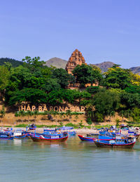 Boats in river by trees against clear blue sky