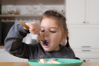 Little child girl sitting at the table and putting spoon at her mouth 
