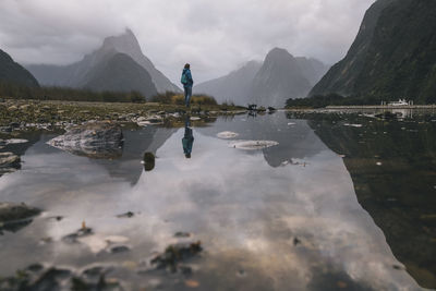 Young woman stands at the view of mitre peak in milford sound, nz