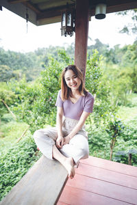 Portrait of smiling woman sitting on railing against trees