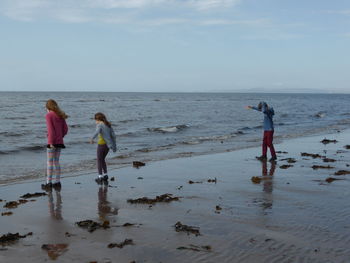 Friends enjoying on sea shore against sky