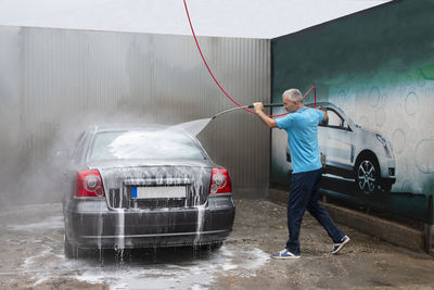 Mature man cleaning automobile with foam shampoo chemical detergents during carwash self service