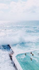 Aerial view of people enjoying in swimming pool by sea