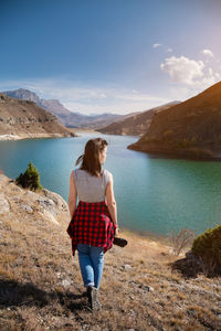 Back view young woman photographer with a photo camera in her hand stands on the shore of a high 