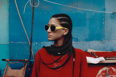 Portrait of young woman wearing sunglasses against wall