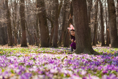 Woman with purple flowers on field by trees in forest