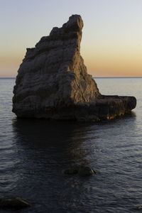 Rock formation in sea against sky at sunset