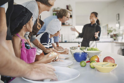 Happy woman talking to family preparing food at table in kitchen