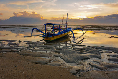 Fishing boat on beach against sky during sunset