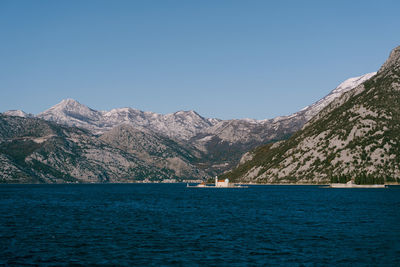 Scenic view of sea and mountains against clear blue sky