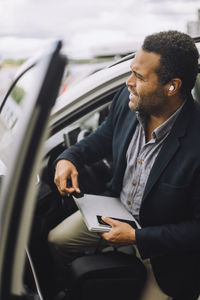 Businessman with laptop and smart phone disembarking from car